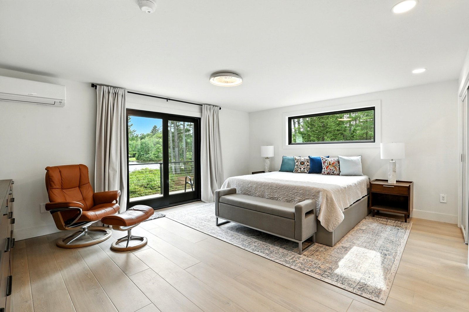 Primary suite with king bed, sliding door to a lakeside deck, and pale oak floors