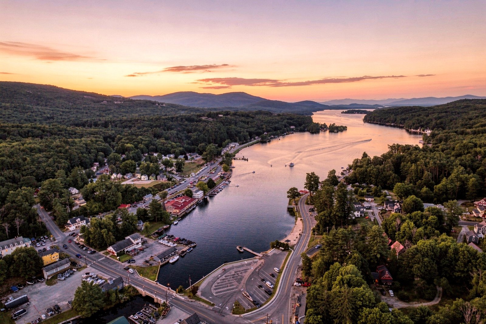 Aerial drone still of a lakeside town at sunset with harbor, boats, and mountains