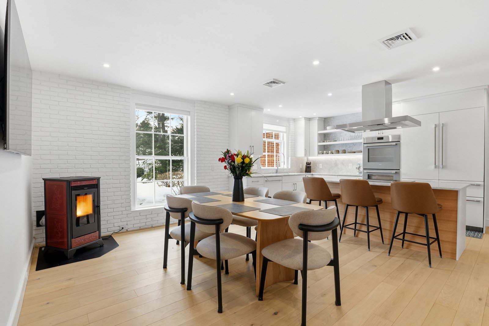 Open-plan kitchen and dining room with white brick hearth, pellet stove, and light oak floors