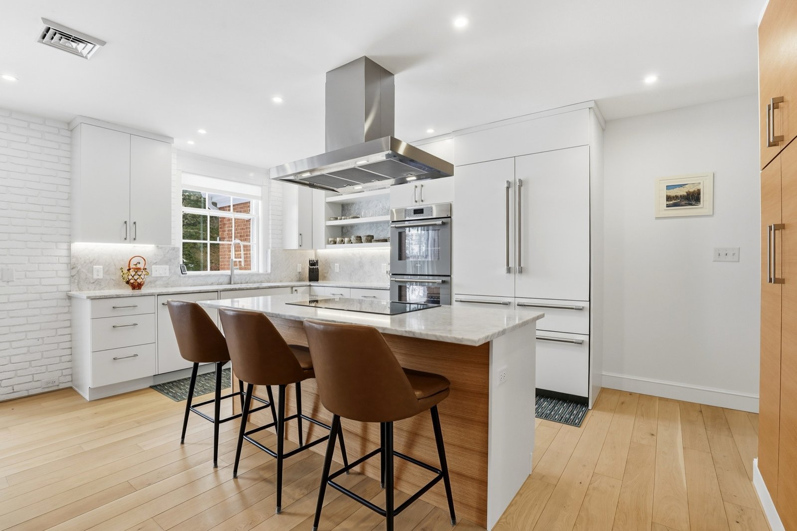 Modern white kitchen with marble island, leather stools, and stainless hood